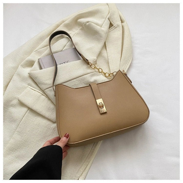 Beige handbag with gold accents held by a hand on a light background