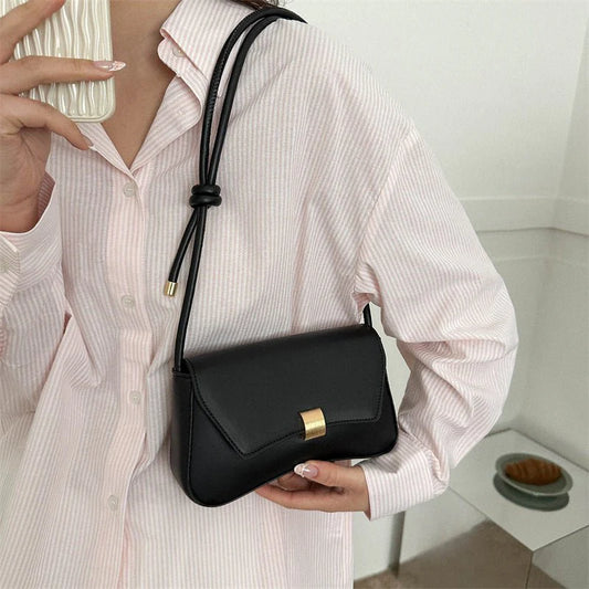 Person holding a black handbag with a gold clasp in a minimal indoor setting